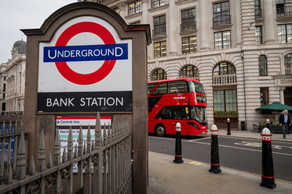 Sign for Bank Station in London, with a red double-decker bus passing.