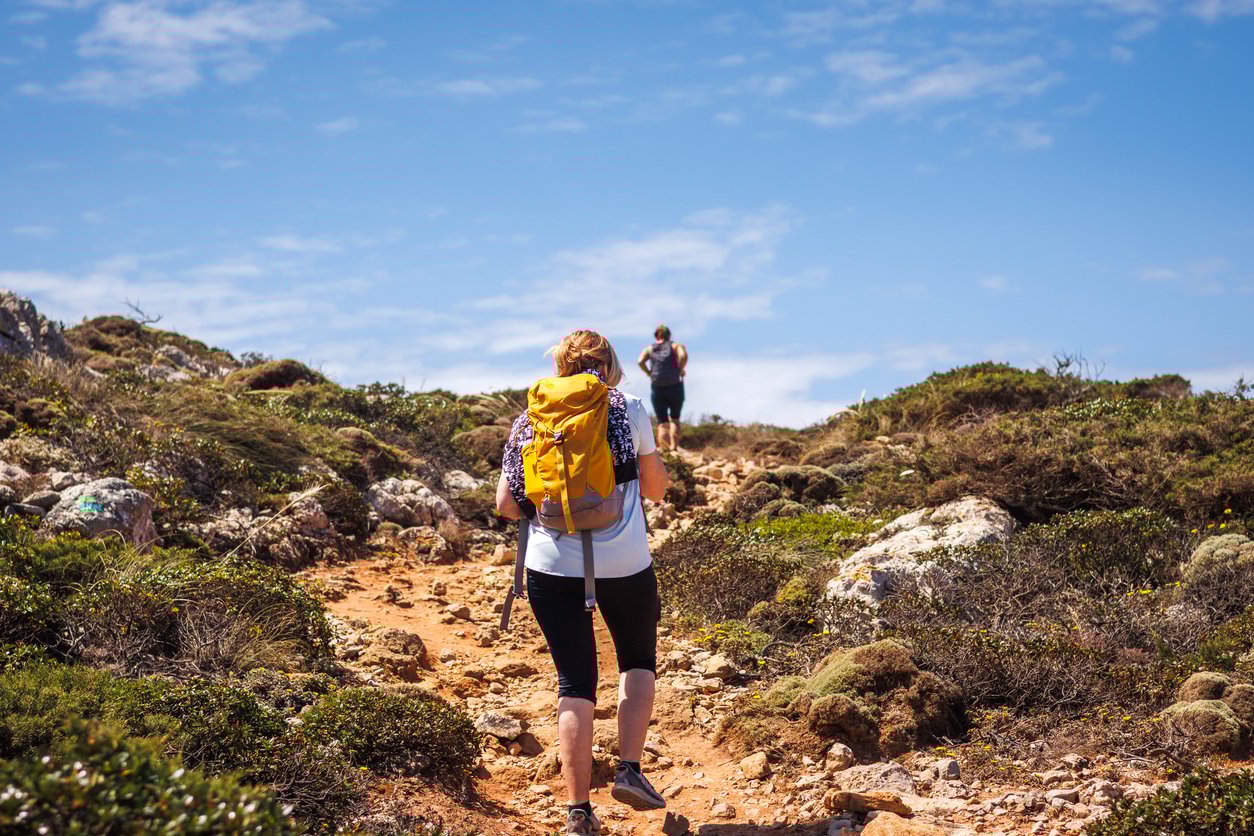 Two people hiking on a rocky trail under a clear blue sky.