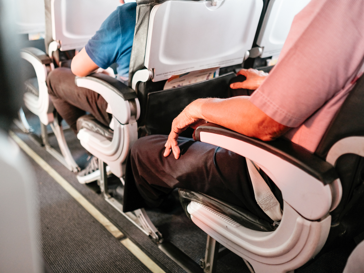 Two people sitting on an airplane with their elbows resting on armrests.