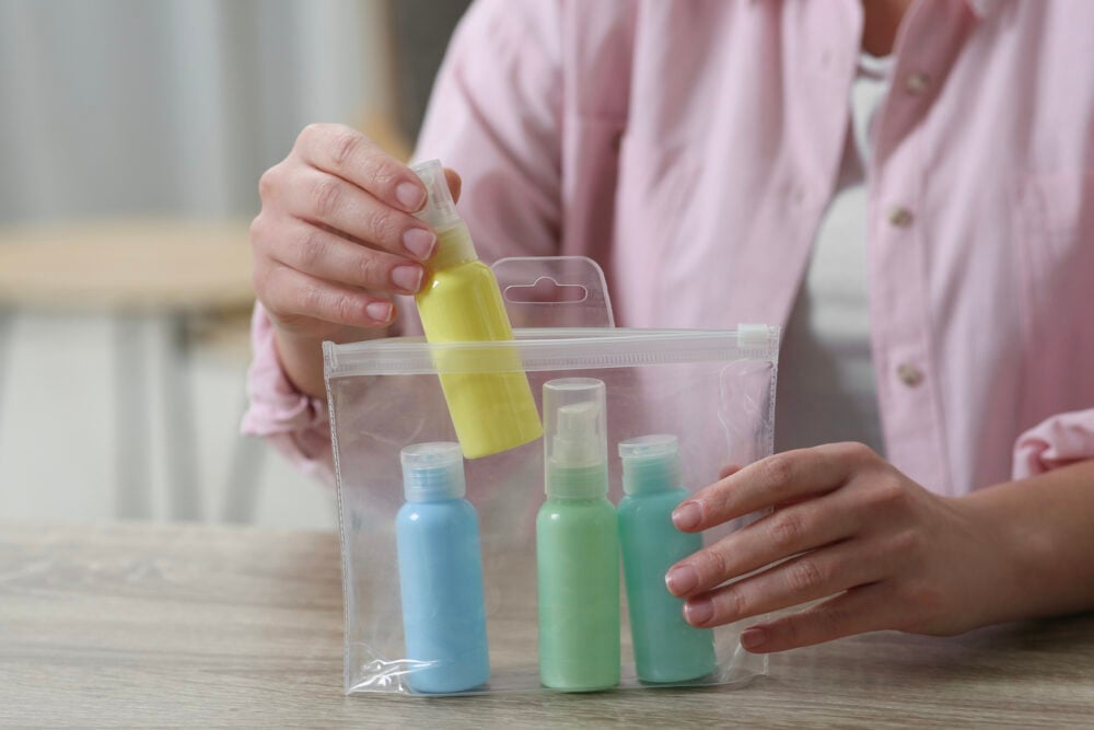 Person placing yellow bottle in clear plastic bag with blue and green bottles inside.