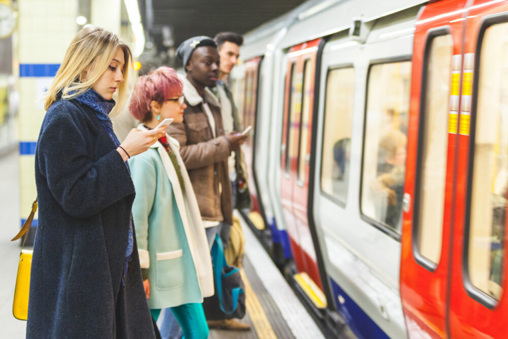 People standing on subway platform next to train, using their phones.