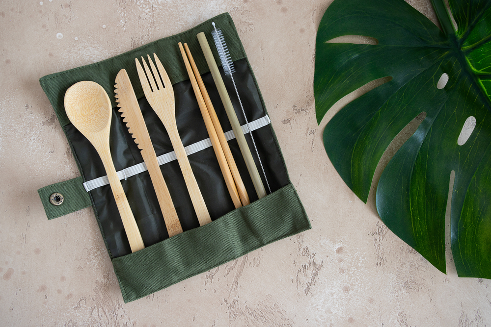 Reusable bamboo cutlery set in a green canvas pouch next to a large green leaf.
