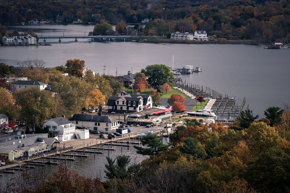 Aerial view of a lakeside village with docks, autumn trees, and residential buildings near the water.