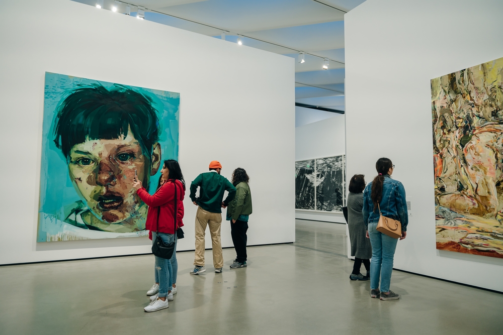 People viewing large paintings in a modern art gallery setting.