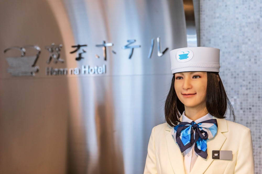 A humanoid robotic receptionist at Henn na Hotel, wearing a white uniform and hat with a blue scarf.