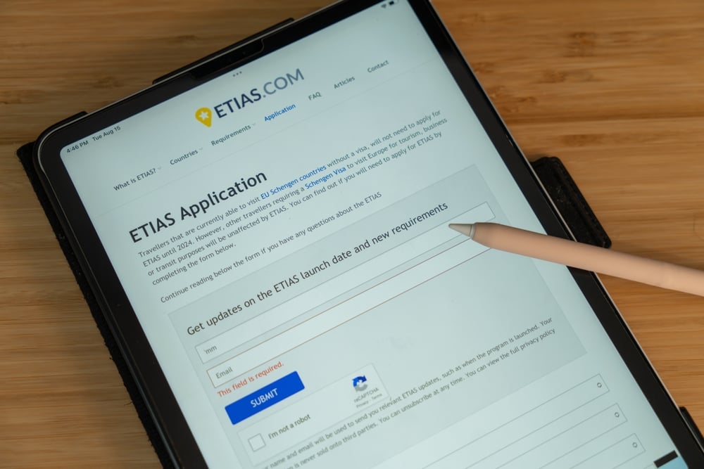 Tablet displaying ETIAS application form with a stylus pointing at the screen.