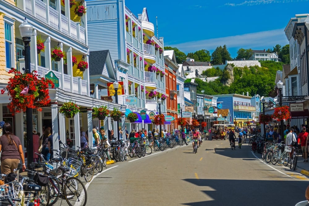 Crowded street lined with colorful buildings and bicycles, people walking, and a hill with buildings in background.