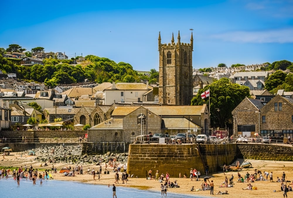 A coastal town with people on a beach, stone buildings, and a church with a tall tower.