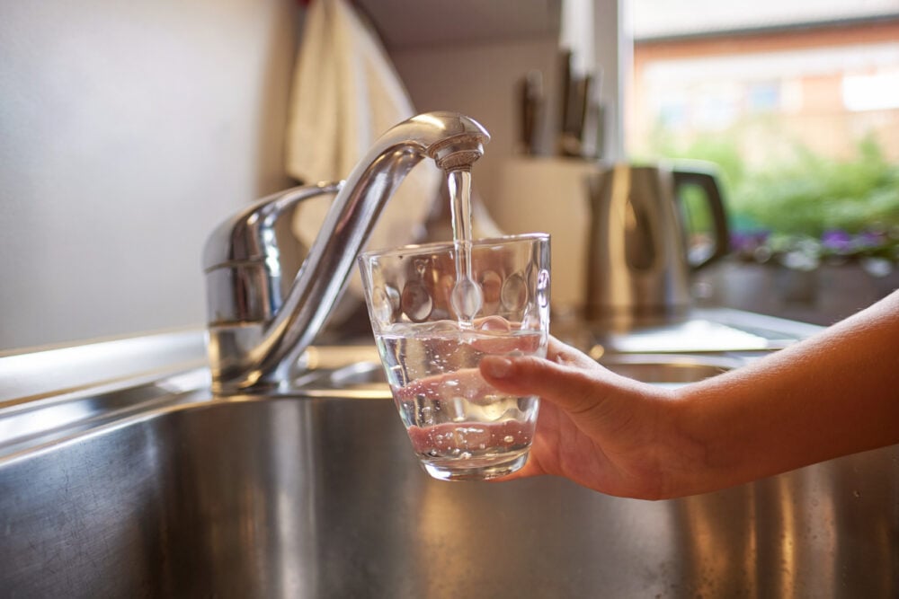 A hand holding a glass under a faucet with water flowing into it.