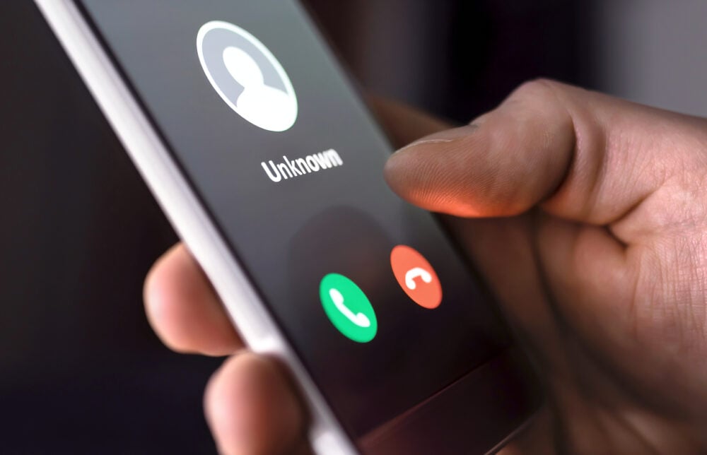Hand holding smartphone displaying incoming call from "Unknown" with green and red call buttons.
