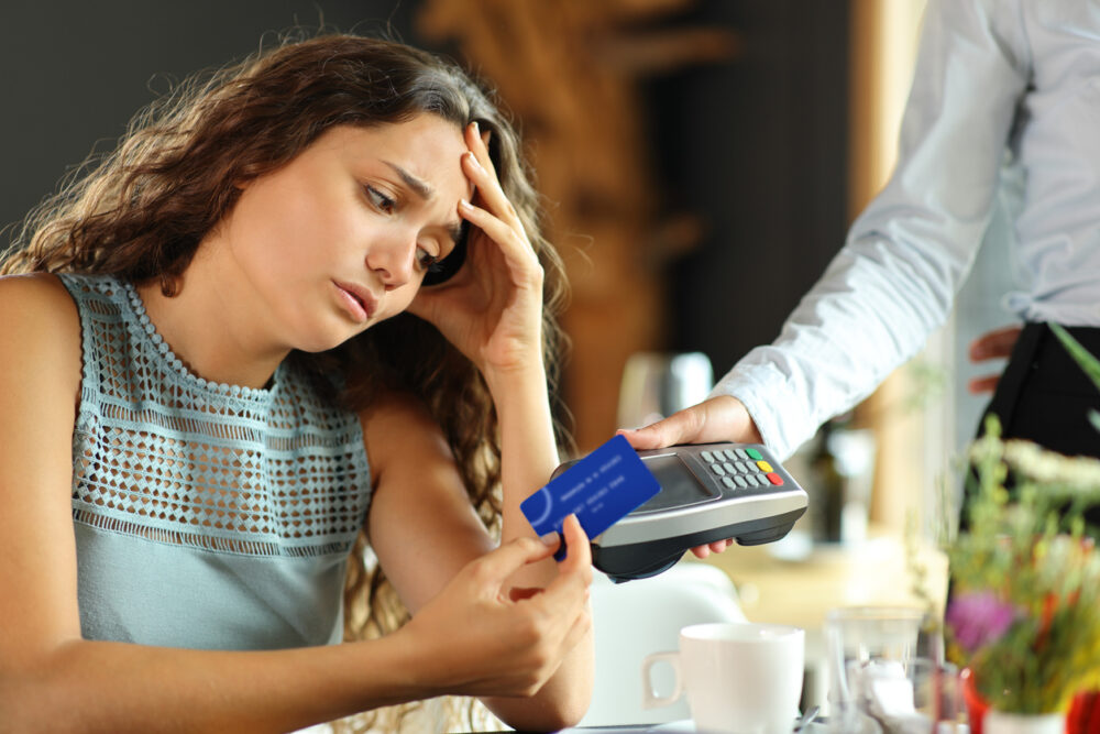 Woman holding credit card with worried expression, facing a payment terminal.