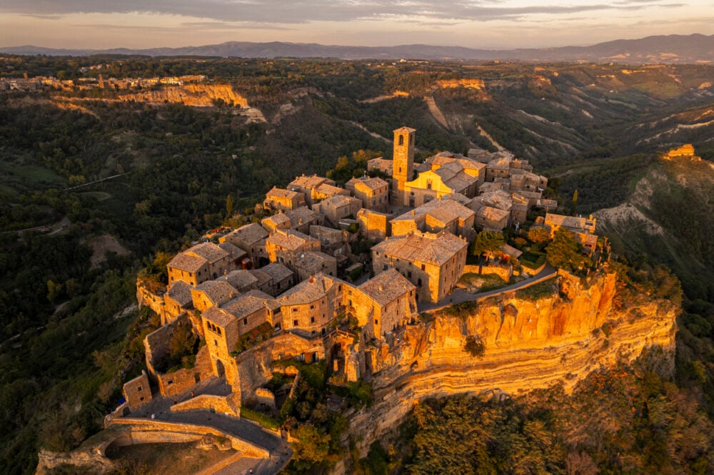 Aerial view of an ancient hilltop village with stone buildings and a central tower at sunset.