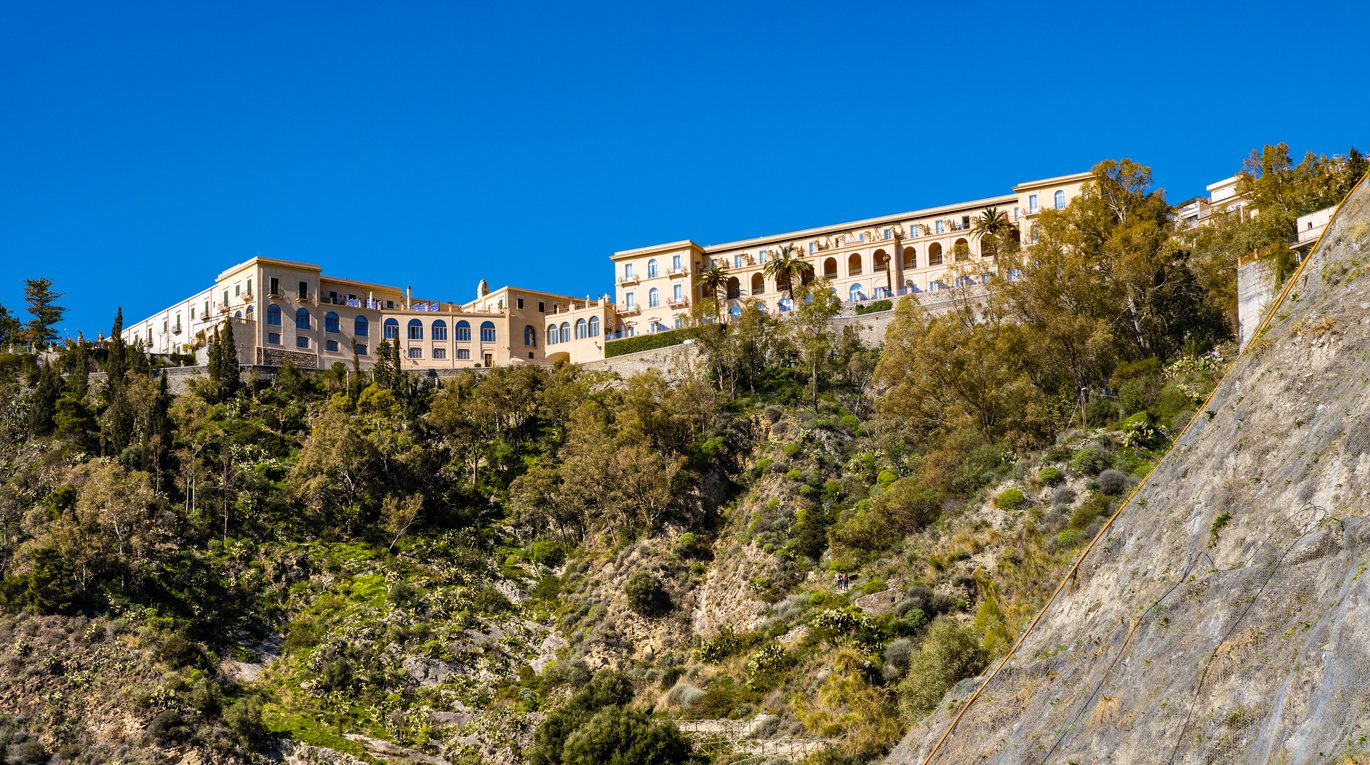 Large building on a hill surrounded by trees under a clear blue sky.