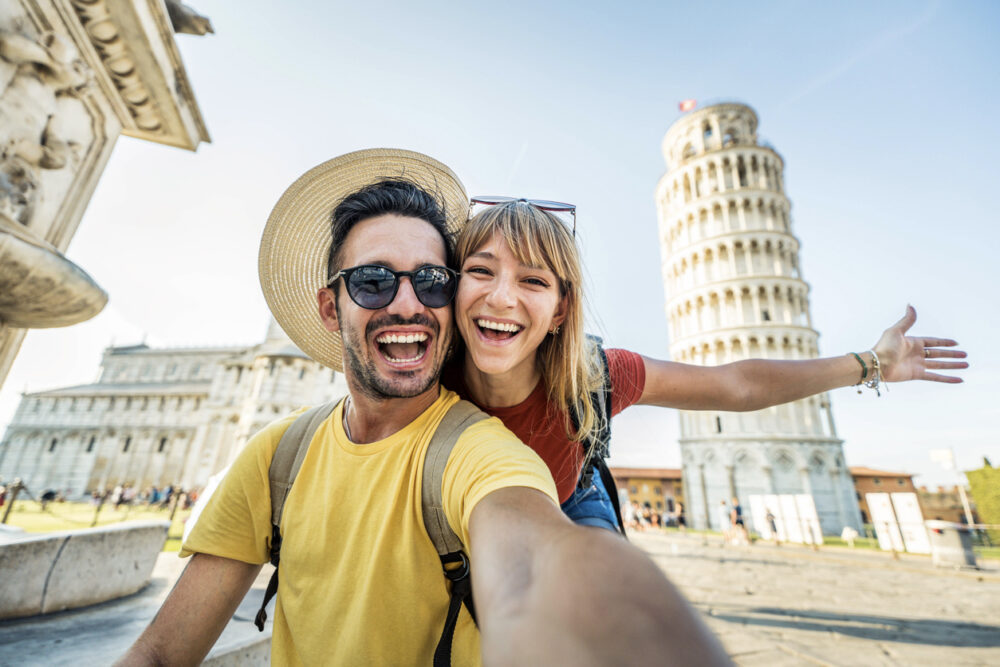 A man and woman taking a selfie in front of the Leaning Tower of Pisa.