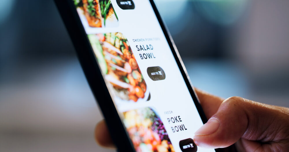 Close-up of a hand browsing a menu on a smartphone, showing salad and poke bowl options.
