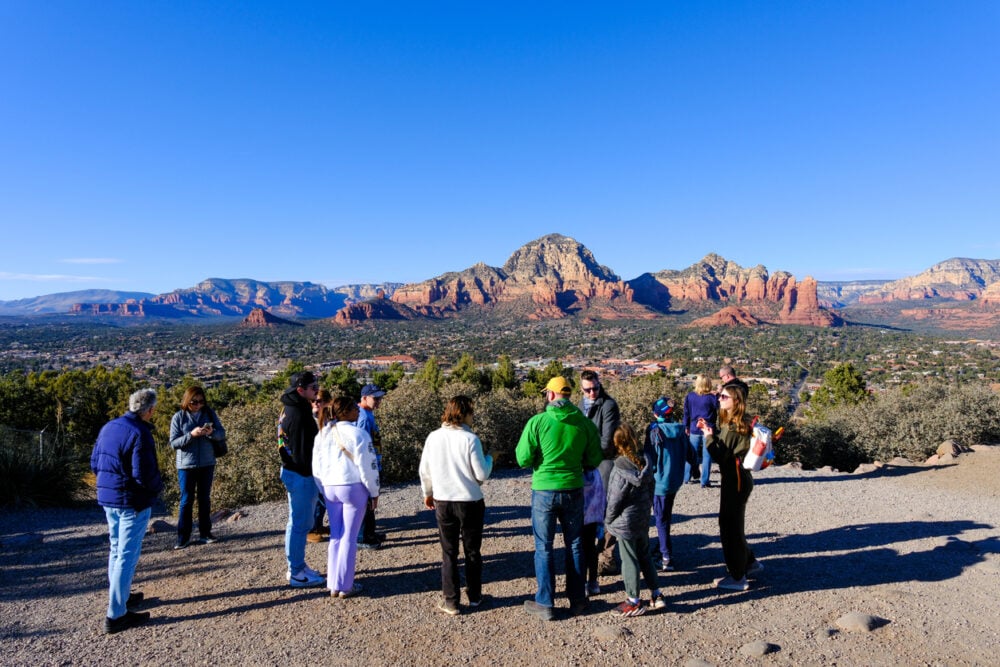 A group of people stands on a hill with Sedona's red rock formations in the background.