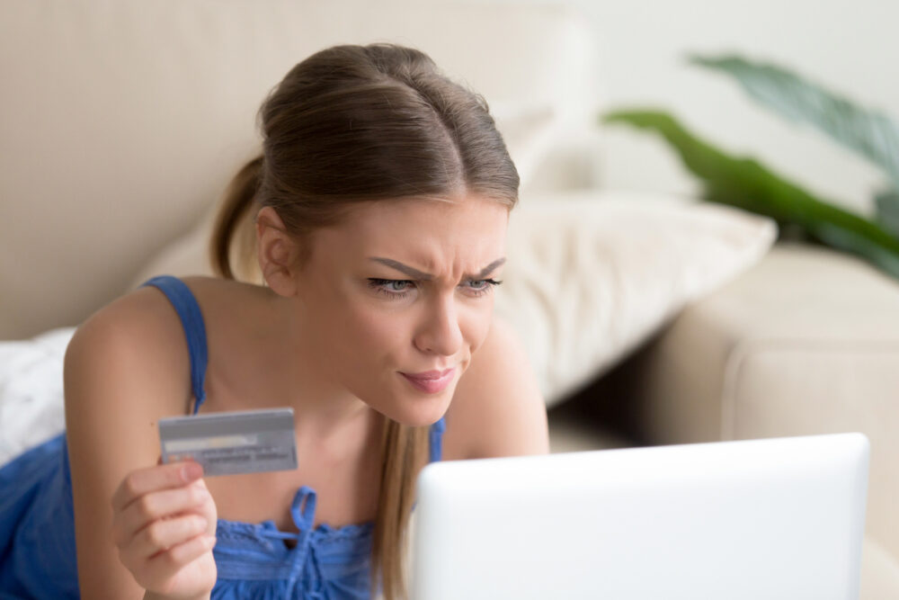 A woman holding a credit card, looking at a laptop screen with a concerned expression.