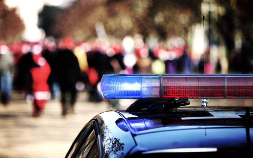 Close-up of police car roof with blue and red lights, blurred crowd in background wearing red hats.