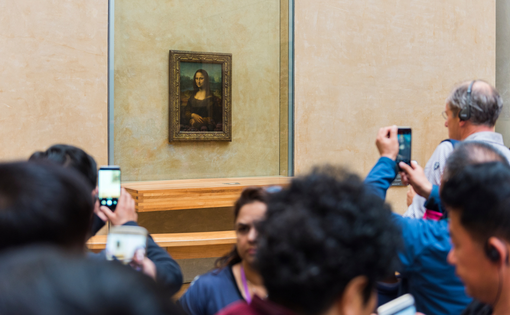 Crowd taking photos of the Mona Lisa painting in a museum gallery.