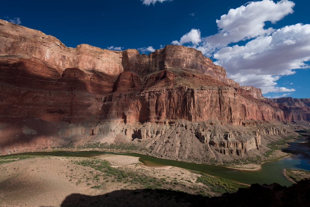 Red rock canyon with river below under a blue sky with scattered clouds.