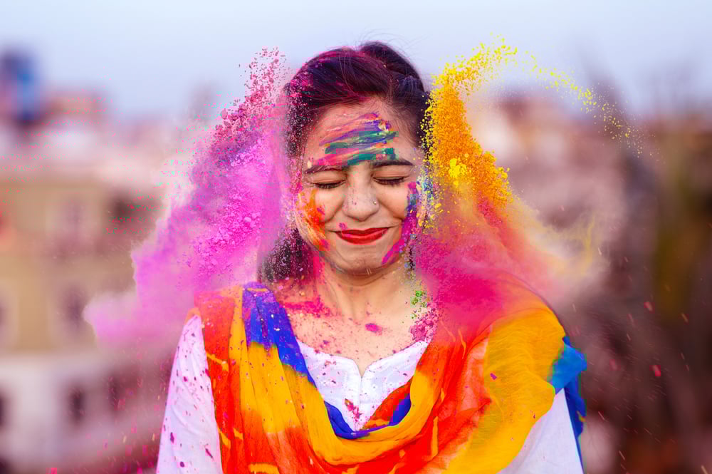 A woman squints as colorful powder bursts around her during a Holi celebration.