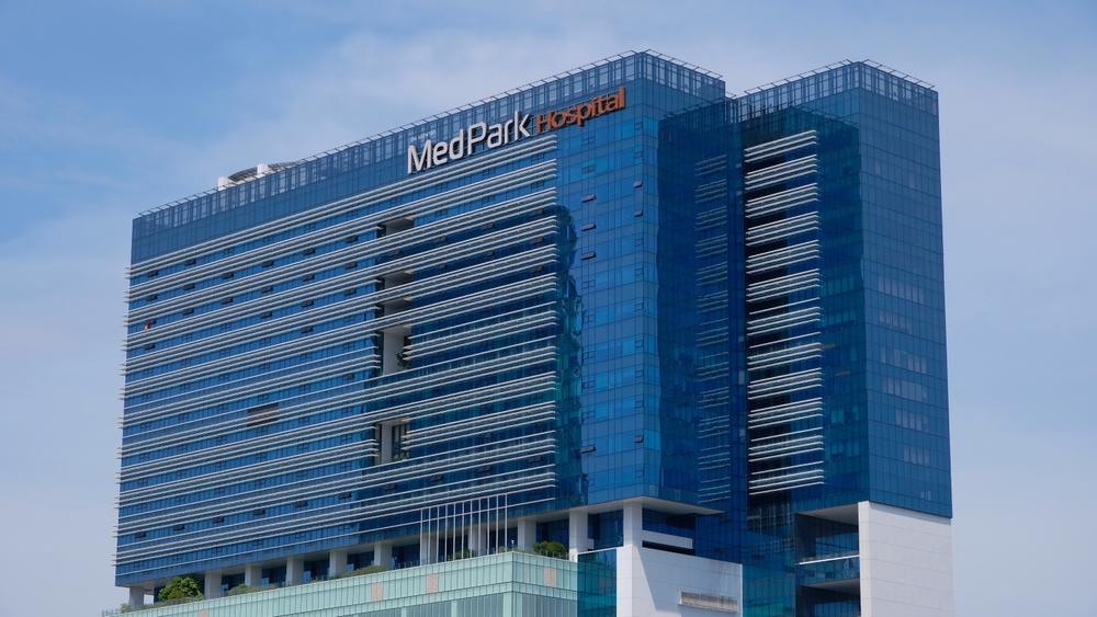 Modern glass building with "MedPark Hospital" signage, featuring blue reflective windows and a clear sky background.