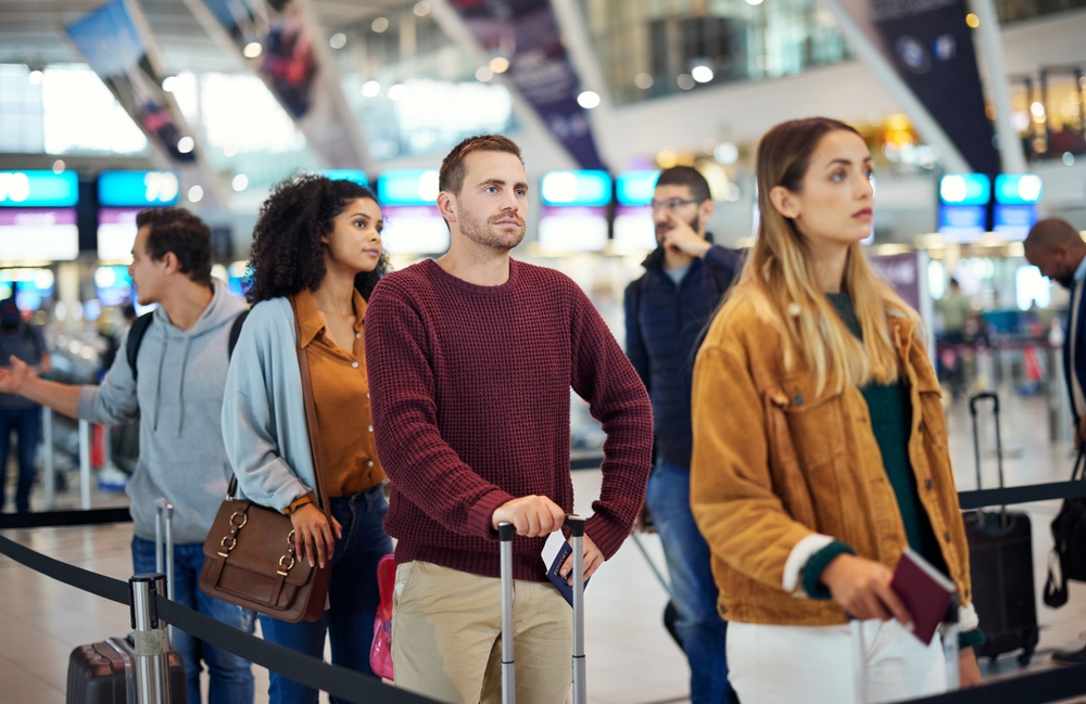 People with luggage standing in line at an airport terminal check-in area.