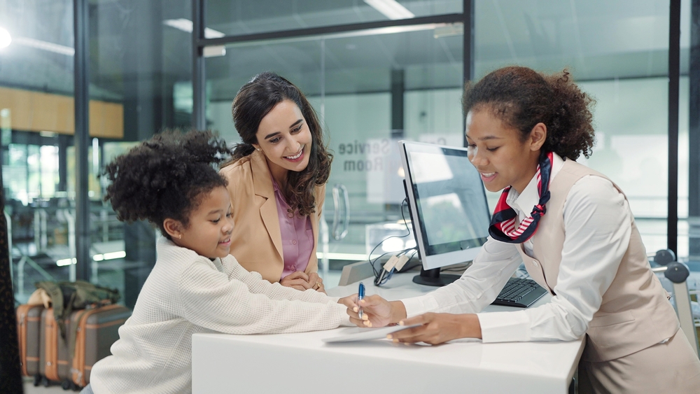 A child and woman at a reception desk with a staff member writing on a paper.