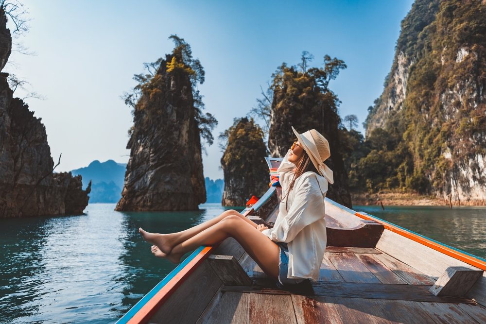 Woman in a hat sitting on a boat, surrounded by rocky islets and calm water.