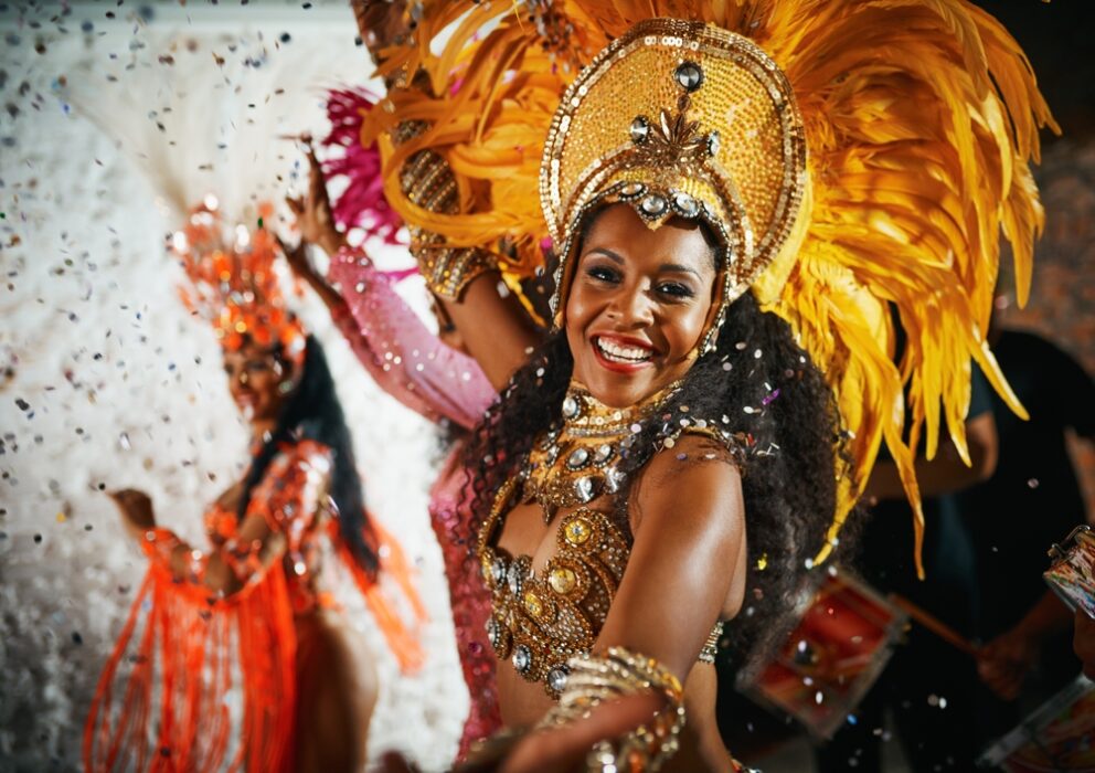 Woman in colorful feathered carnival costume, smiling, surrounded by confetti.