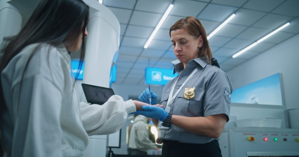 Security officer swabbing woman's hand at airport checkpoint for security screening in a brightly lit area.