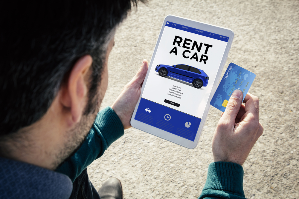Man holding tablet displaying car rental app and credit card in hand.