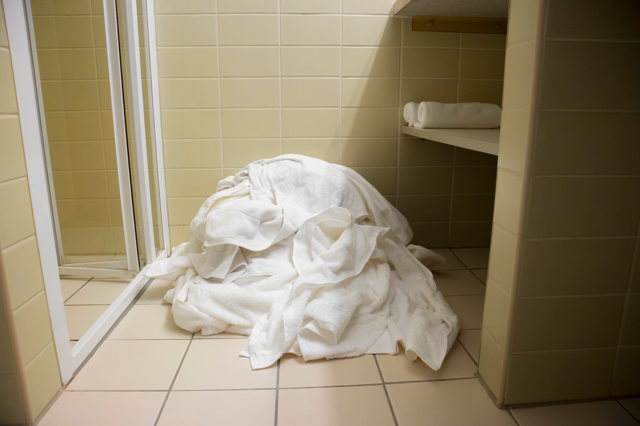 Pile of white towels on tiled bathroom floor next to shower door.