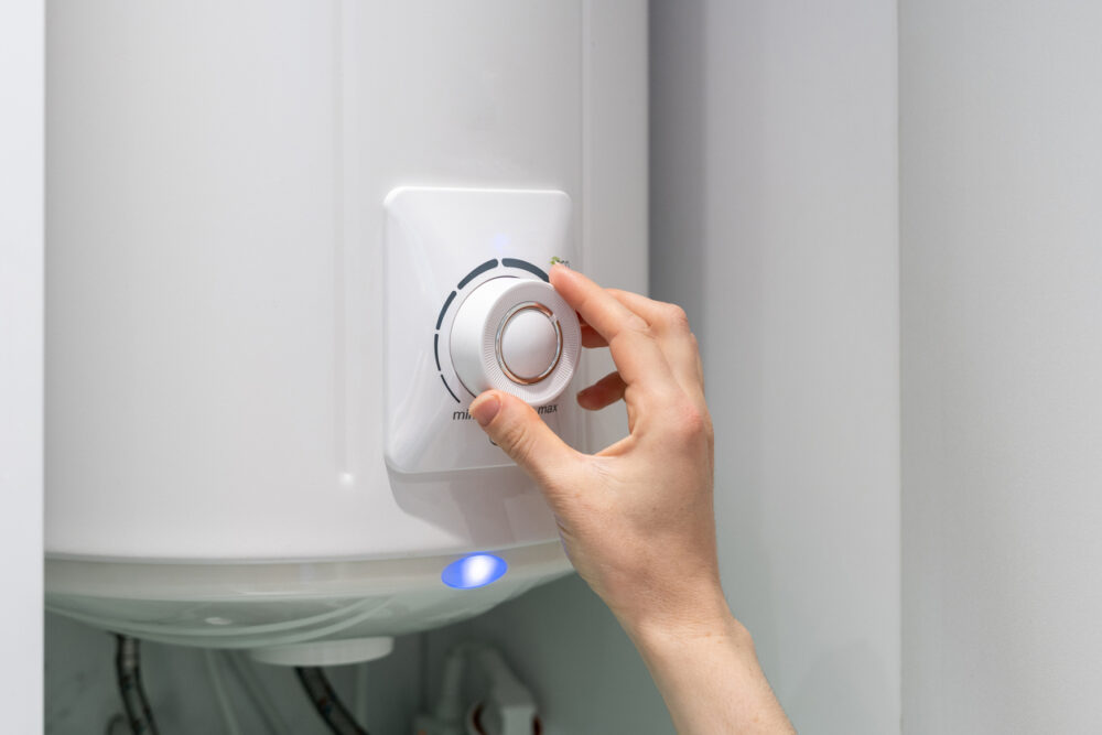 Hand adjusting the temperature dial on a white water heater unit.