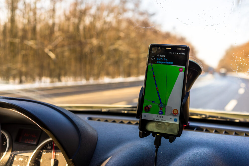 Smartphone displaying GPS navigation in a car mount with a view of the road through the windshield.