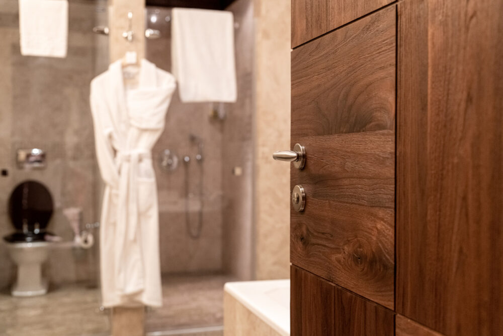 Wooden bathroom door open, revealing a robe, towels, and shower in the background.