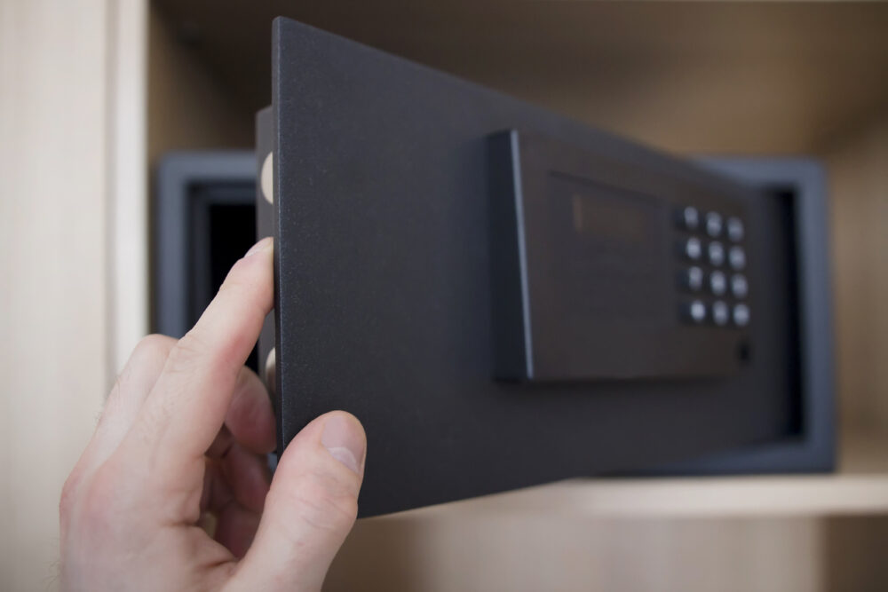 Hand opening a black safe with a keypad.