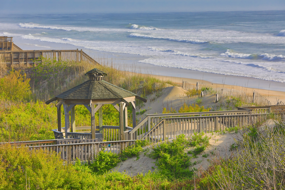 Wooden gazebo and boardwalk leading to sandy beach with ocean waves in the background.