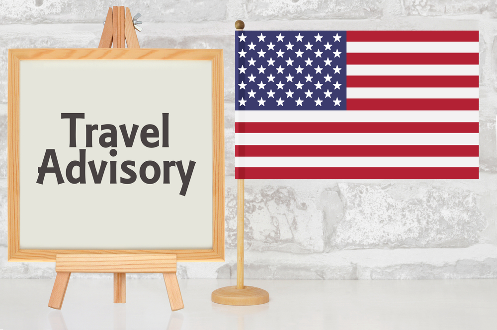 Easel with "Travel Advisory" sign, next to small United States flag on a stand.