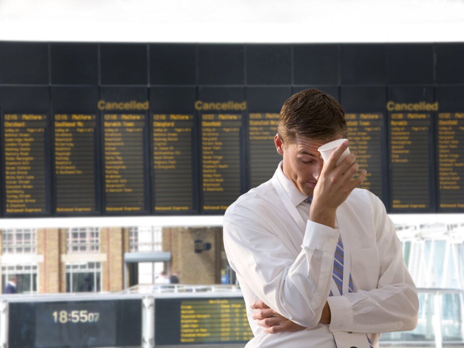 Man in white shirt holds face near train station cancellation board.
