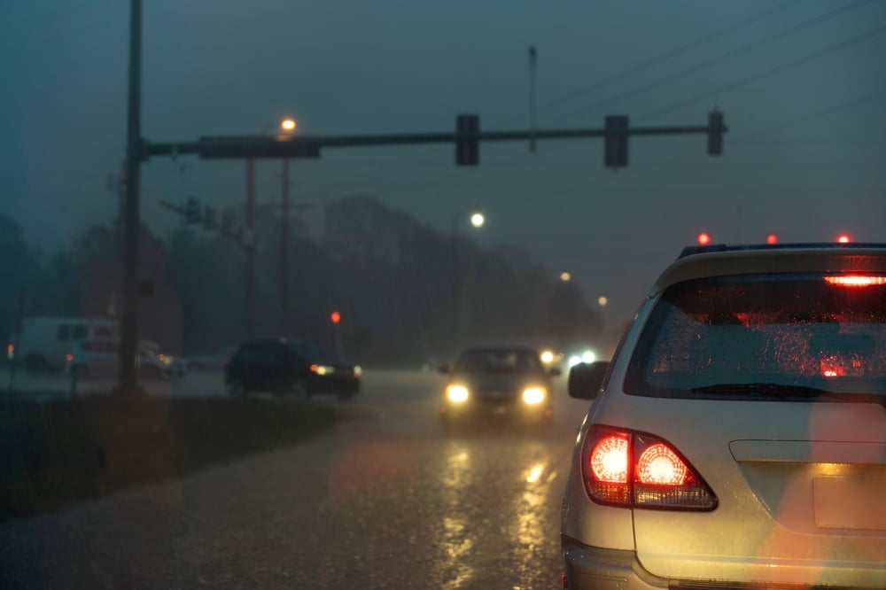 A car stopped at a traffic light in heavy rain, with blurry headlights of oncoming vehicles.