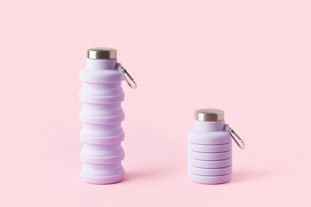 Purple collapsible water bottles with metal caps and carabiners on a pink background.