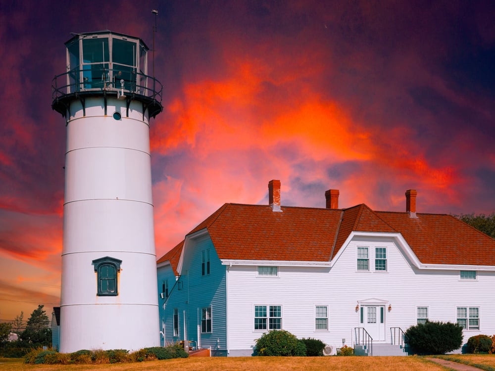 White lighthouse and building with red roof against vibrant sunset sky.