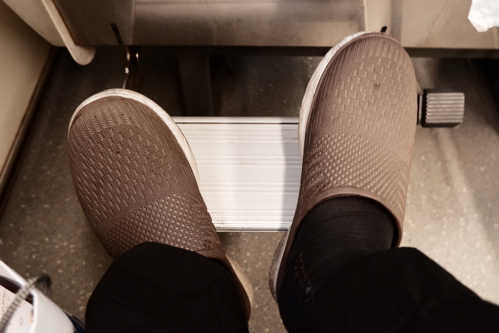 Brown shoes on footrest inside a vehicle, with black pants and black socks visible.