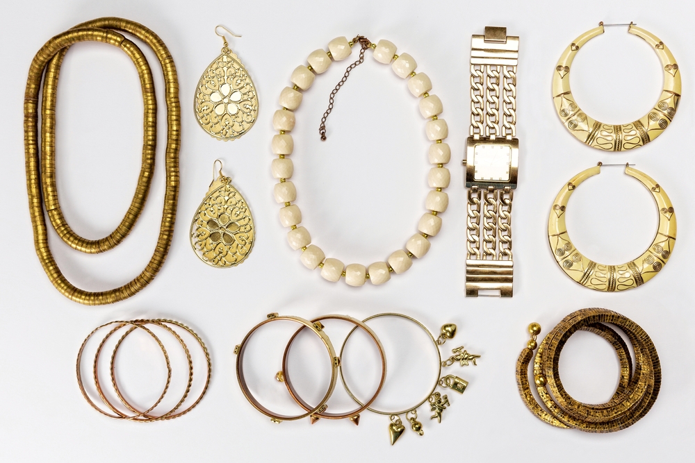 Assorted jewelry including gold necklaces, bracelets, hoop earrings, a watch, and decorative earrings on white background.