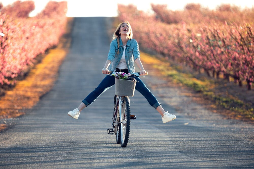 Person riding a bicycle with legs extended, on a road lined with blooming trees.