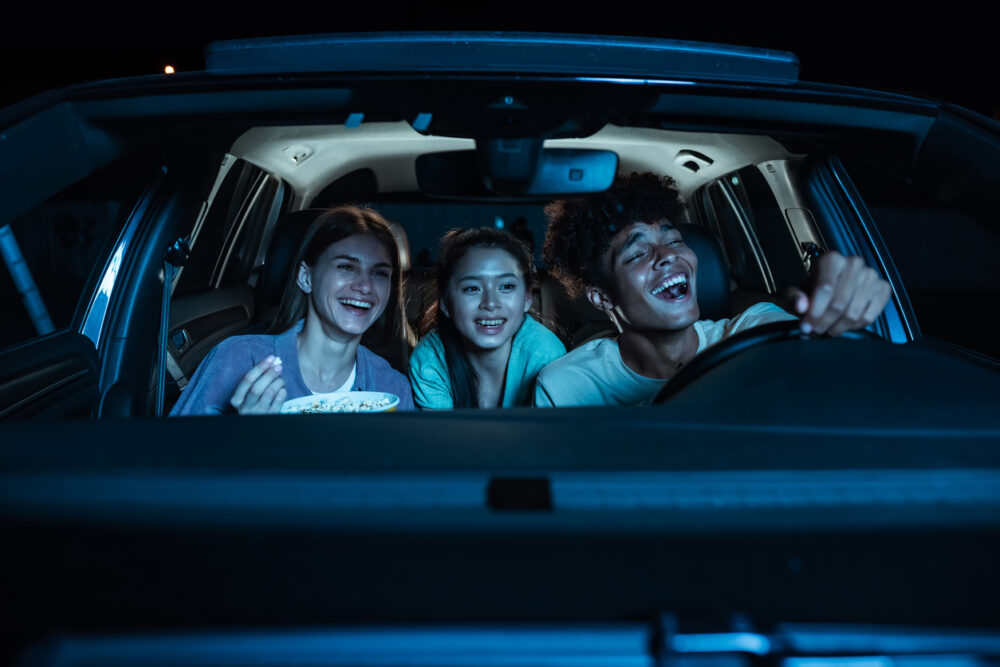 Three young people in a car at night, laughing and eating popcorn together.