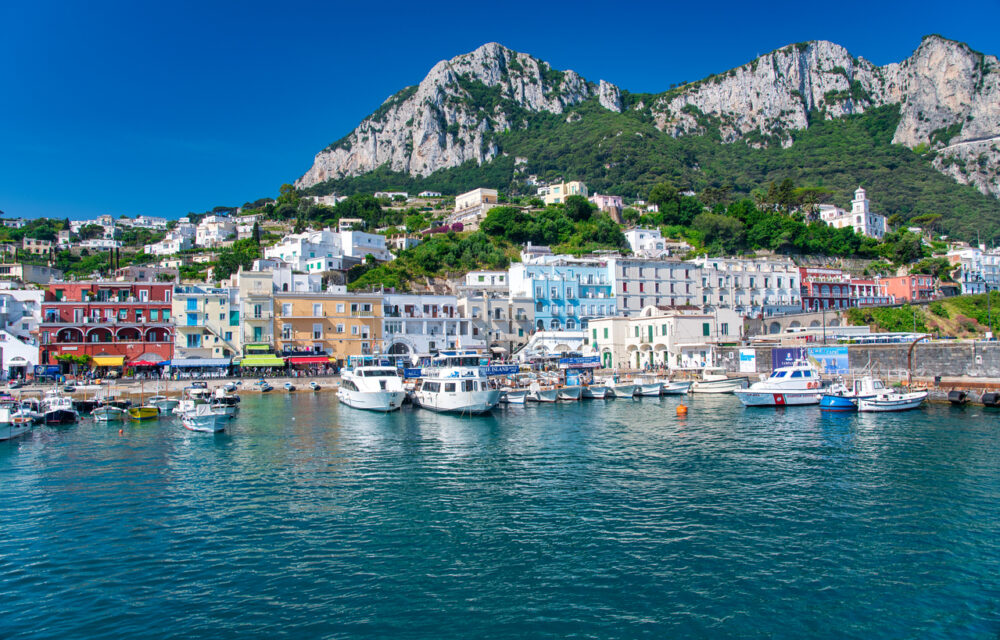 Colorful buildings and boats in a harbor with a mountainous backdrop.