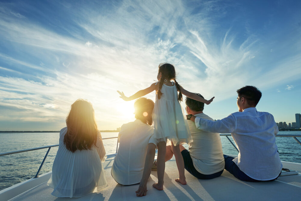Four people sitting and one child standing on a boat, with sunset over the water.