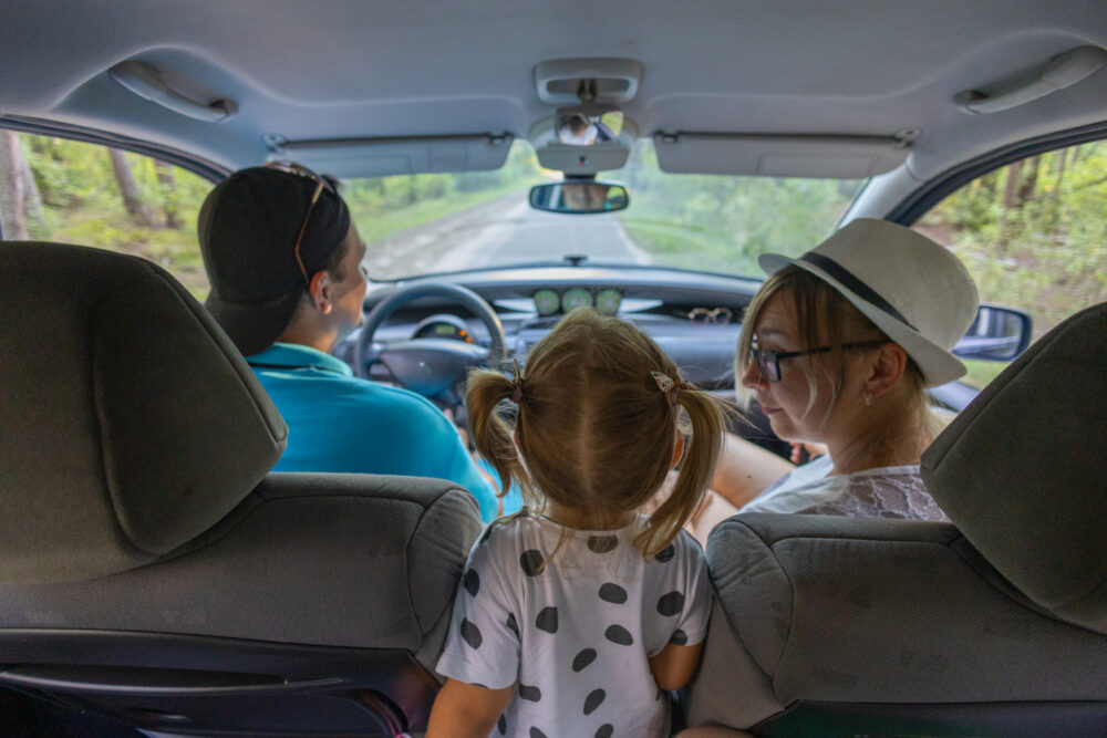 Child with pigtails seated between two adults in a moving car, view from the backseat.
